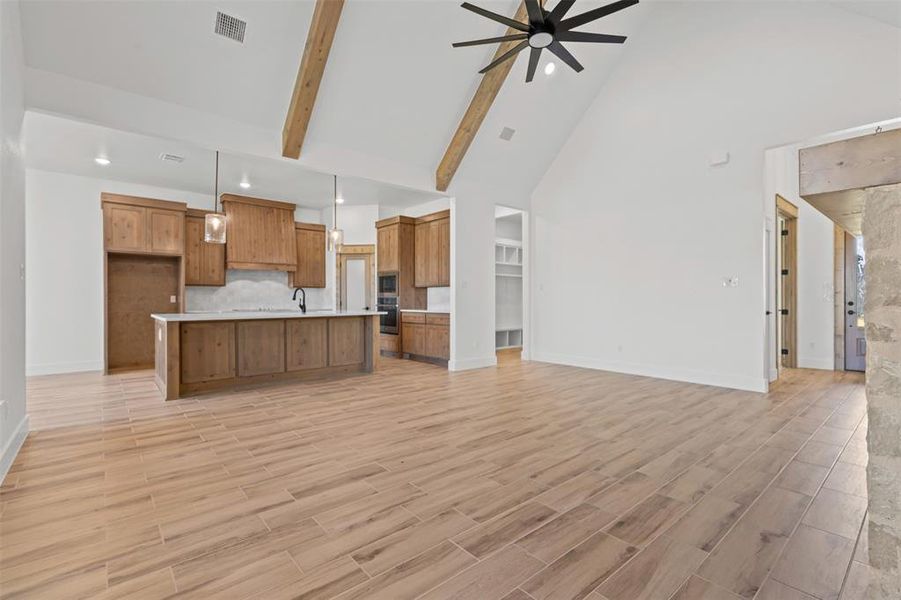 Kitchen featuring open floor plan, high vaulted ceiling, pendant lighting, brown cabinetry, and a spacious island