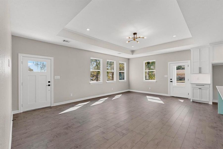 Unfurnished living room featuring a chandelier, a tray ceiling, and dark wood-type flooring Unfurnished living room featuring a chandelier, a tray ceiling, and dark wood-type flooring