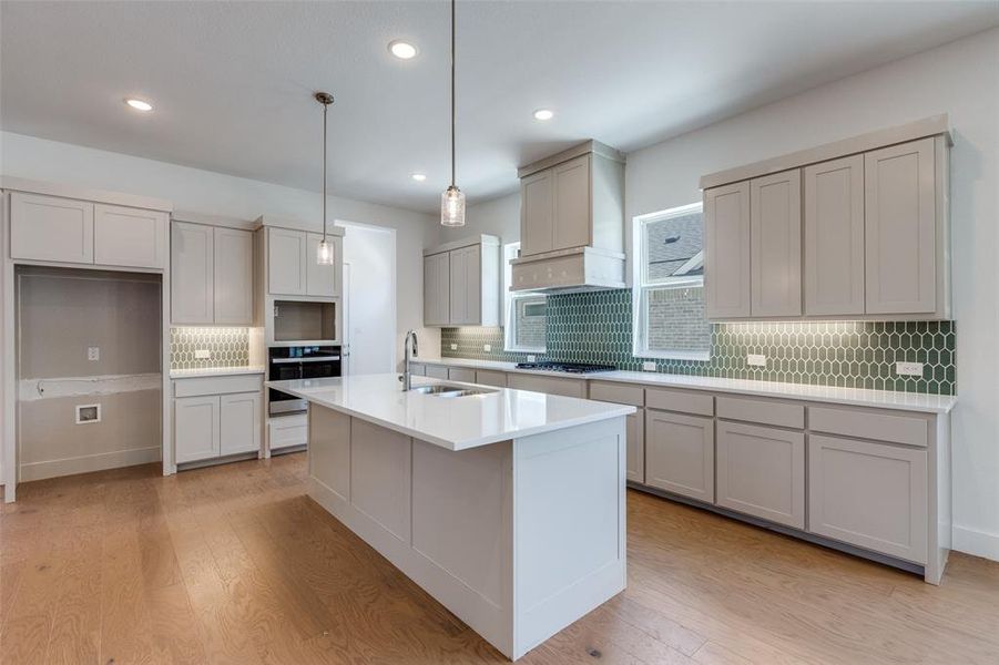 Kitchen featuring custom exhaust hood, stainless steel appliances, a center island with sink, light wood-type flooring, and sink