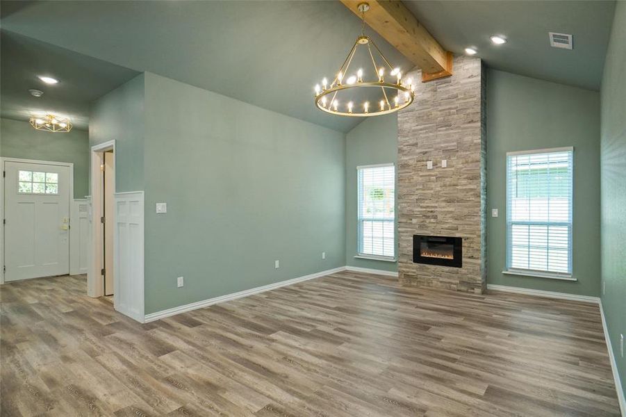 Unfurnished living room featuring beamed ceiling, wood-type flooring, an inviting chandelier, and a fireplace