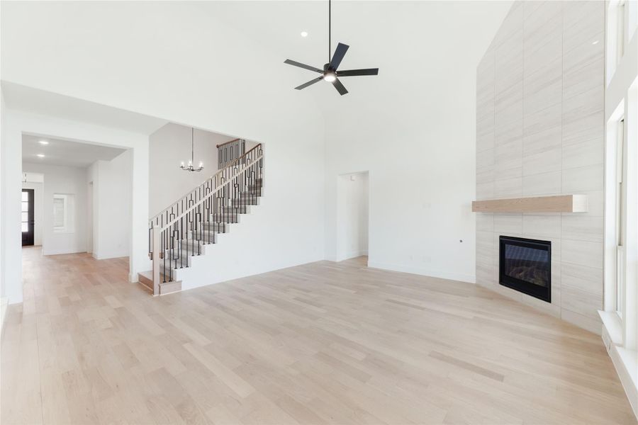 Open living room with vaulted ceiling, tile fireplace, staircase, and light hardwood floors