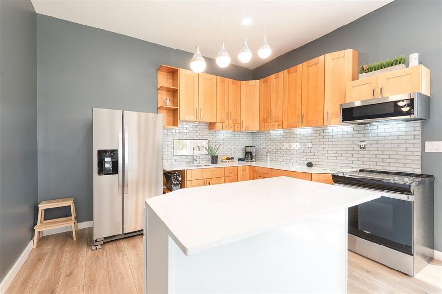 Kitchen featuring appliances with stainless steel finishes, light brown cabinetry, decorative backsplash, and open shelves Kitchen featuring appliances with stainless steel finishes, light brown cabinetry, decorative backsplash, and open shelves