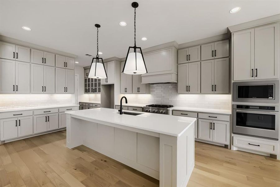 Open-concept kitchen featuring light-toned cabinetry, a spacious center island with a white countertop, stainless steel appliances, and wood-finish flooring Open-concept kitchen featuring light-toned cabinetry, a spacious center island with a white countertop, stainless steel appliances, and wood-finish flooring
