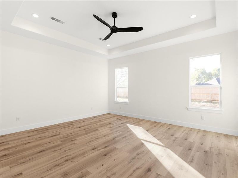 Empty room featuring light wood-type flooring, a raised ceiling, a ceiling fan, and recessed lighting