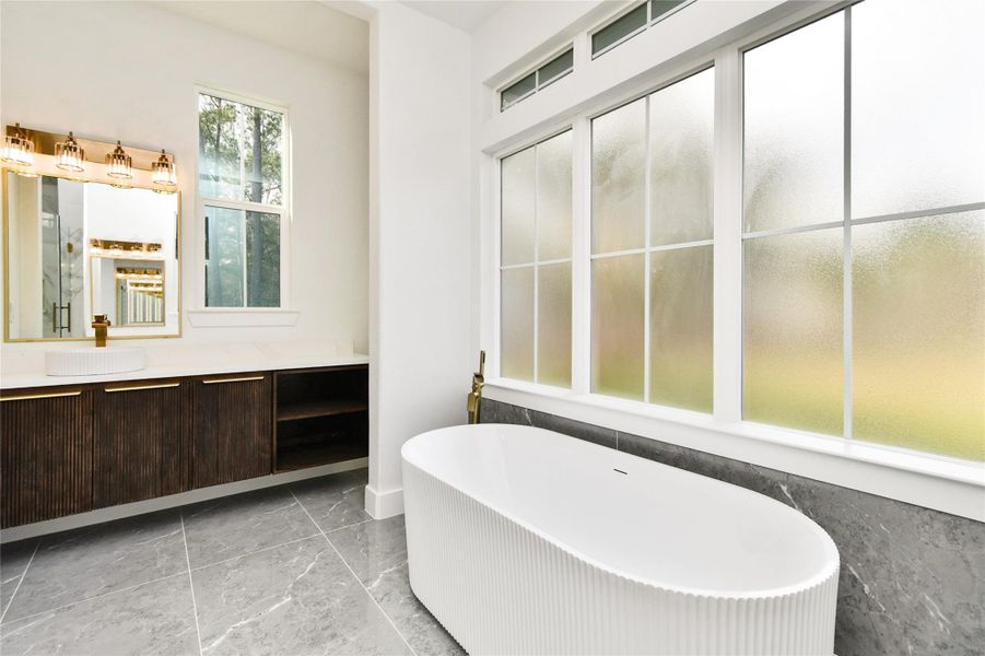 Relax in the deep freestanding soaking tub, positioned under large windows with frosted privacy glass.