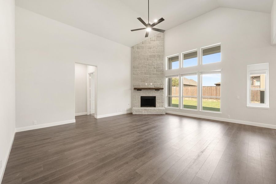 Open living room with vaulted ceiling, floor-to-ceiling stone fireplace, dark hardwood floors, and large windows Open living room with vaulted ceiling, floor-to-ceiling stone fireplace, dark hardwood floors, and large windows