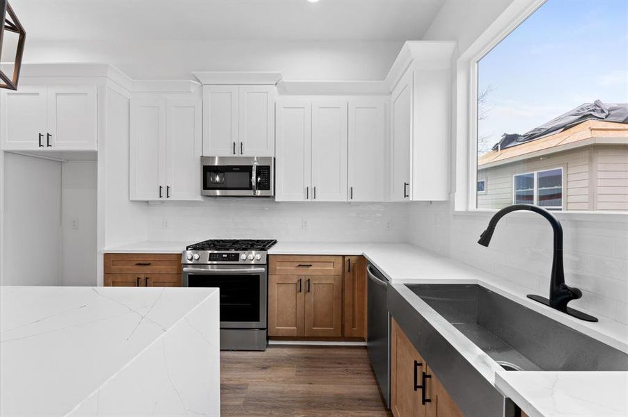 Modern kitchen with white upper cabinets and wood lower cabinets, featuring stainless steel appliances, a large window, and sleek black fixtures. Bright and inviting space with ample countertop area.