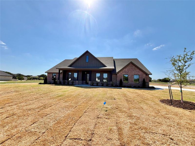 View of front of property featuring board and batten siding, a porch, a front yard, and brick siding View of front of property featuring board and batten siding, a porch, a front yard, and brick siding