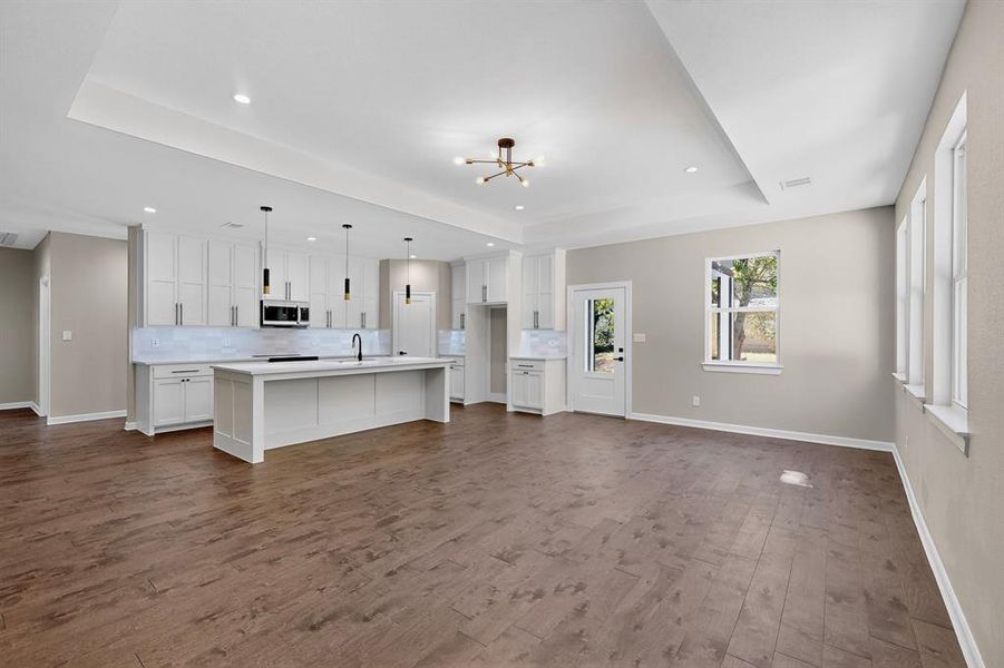 Kitchen featuring a tray ceiling, open floor plan, decorative backsplash, a kitchen island with sink, and dark wood-style floors Kitchen featuring a tray ceiling, open floor plan, decorative backsplash, a kitchen island with sink, and dark wood-style floors