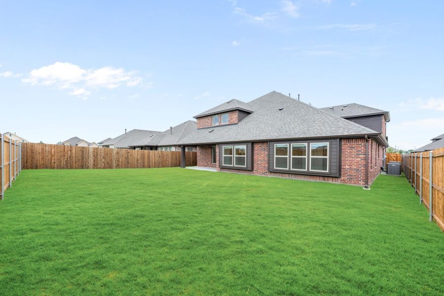 Backyard of brick two-story home with large green lawn and wood privacy fence on both sides. Backyard of brick two-story home with large green lawn and wood privacy fence on both sides.