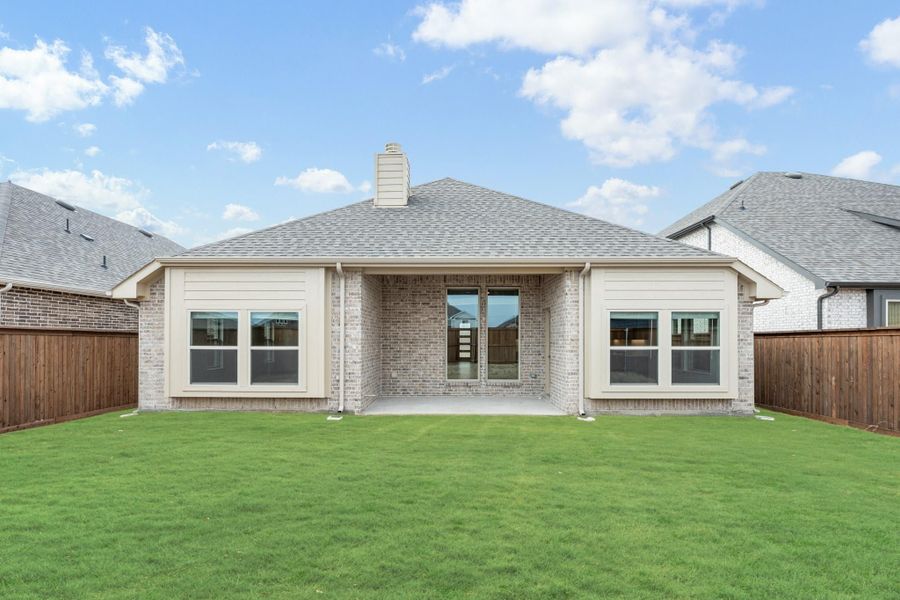 Rear exterior of single-story brick home with covered patio, large windows, and fenced backyard lawn Rear exterior of single-story brick home with covered patio, large windows, and fenced backyard lawn