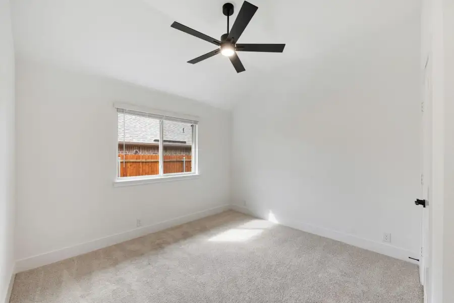 Empty bedroom with vaulted ceiling, black ceiling fan, carpet flooring, and single window