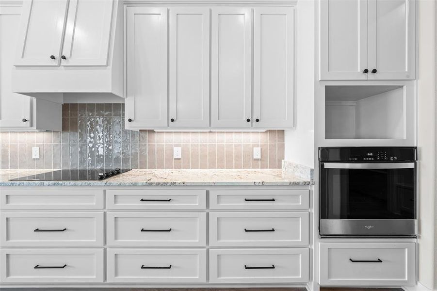 Kitchen featuring white cabinets, oven, light stone countertops, and decorative backsplash