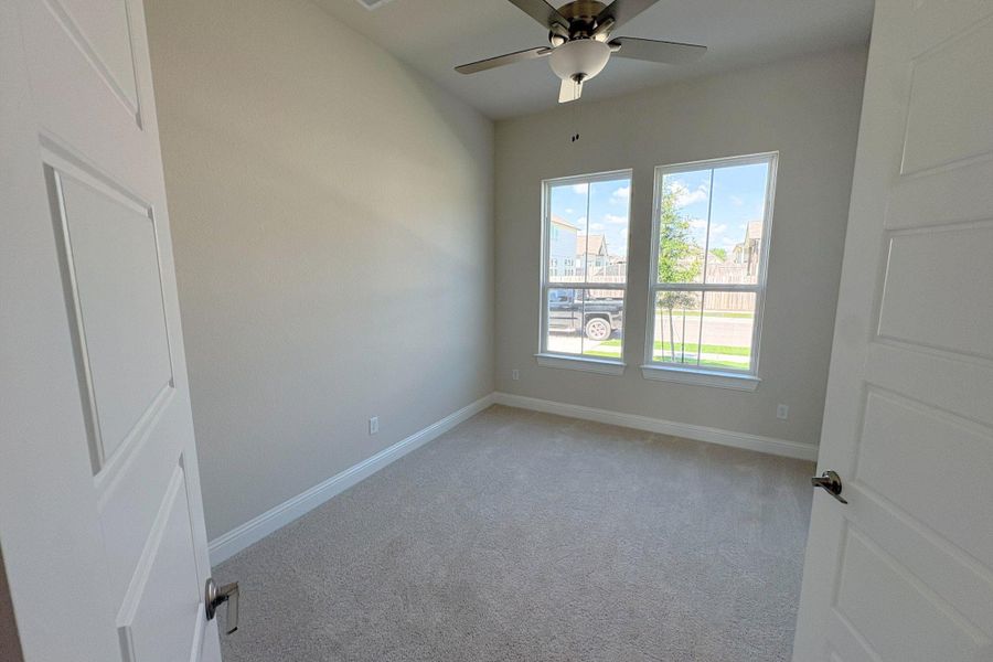 Carpeted room featuring two panel doors, a ceiling fan with integrated lighting, and two double-hung windows with white frames