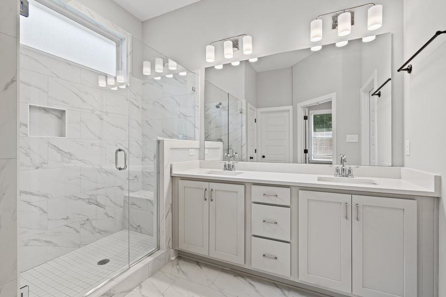 Full bathroom with plenty of natural light, a marble finish shower, light marble finish flooring, and double vanity