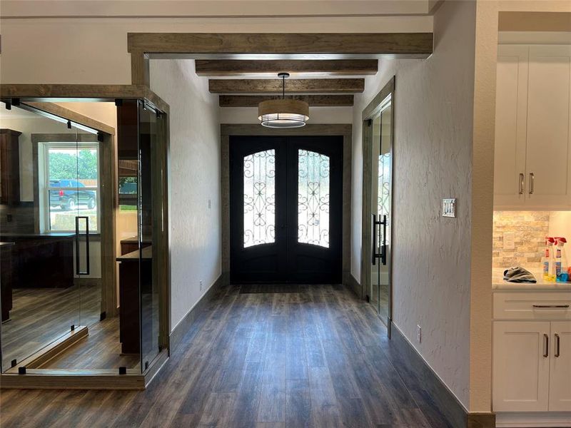 Foyer entrance with baseboards, dark wood finished floors, french doors, beamed ceiling, and a textured wall Foyer entrance with baseboards, dark wood finished floors, french doors, beamed ceiling, and a textured wall