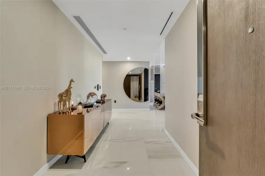 Entryway featuring neutral wall finishes, large-format polished tile flooring, recessed ceiling lighting, and a circular wall mirror Entryway featuring neutral wall finishes, large-format polished tile flooring, recessed ceiling lighting, and a circular wall mirror