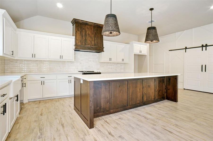 Kitchen featuring decorative light fixtures, a barn door, a center island, light hardwood / wood-style floors, and backsplash