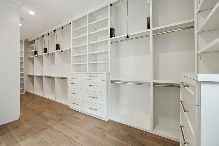 Spacious primary closet features built-in storage and ample room for hanging clothes with pull-down bars for accessing all custom storage solutions.