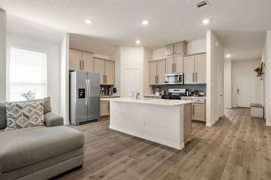 Kitchen featuring appliances with stainless steel finishes, backsplash, an island with sink, light wood-style flooring, and recessed lighting Kitchen featuring appliances with stainless steel finishes, backsplash, an island with sink, light wood-style flooring, and recessed lighting