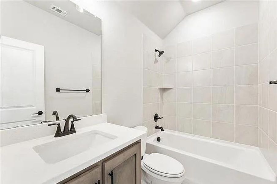 Bathroom with toilet, vanity, shower / tub combination, and vaulted ceiling