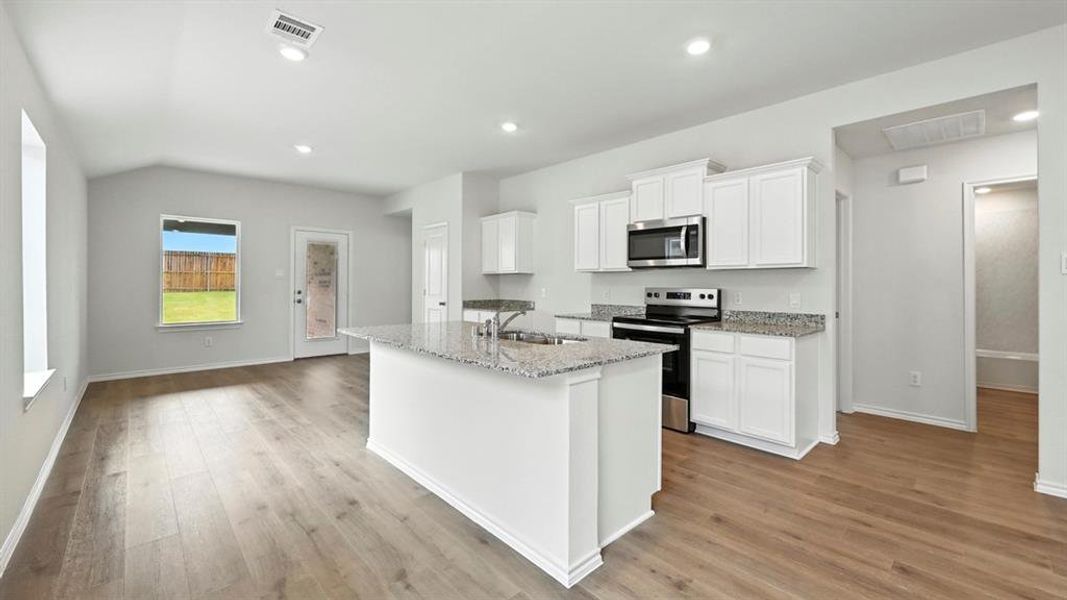 Open-concept living space featuring wood-finish flooring, recessed lighting, and a kitchen island with stone countertops Open-concept living space featuring wood-finish flooring, recessed lighting, and a kitchen island with stone countertops