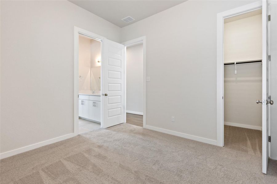 Unfurnished bedroom featuring a spacious closet, light colored carpet, and ensuite bathroom