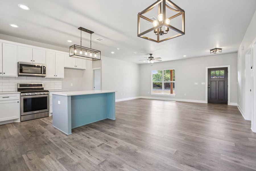 Kitchen featuring a chandelier, pendant lighting, appliances with stainless steel finishes, white cabinetry, and a center island