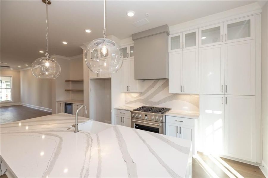 Kitchen with white cabinetry, hanging light fixtures, light stone countertops, high end stainless steel range, and recessed lighting