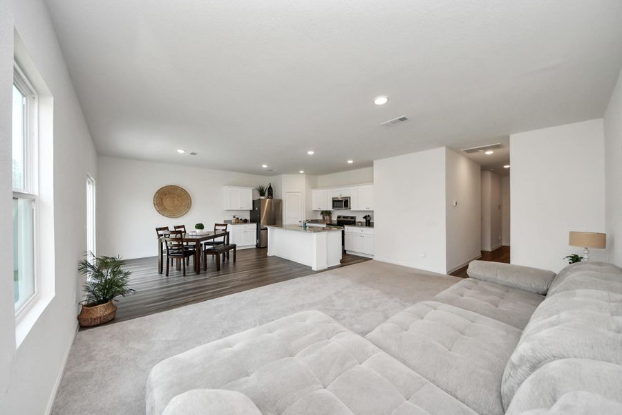 Large open-concept living area with plush carpeting and abundant natural light, seamlessly flowing into a modern kitchen with sleek cabinetry and stainless steel appliances.