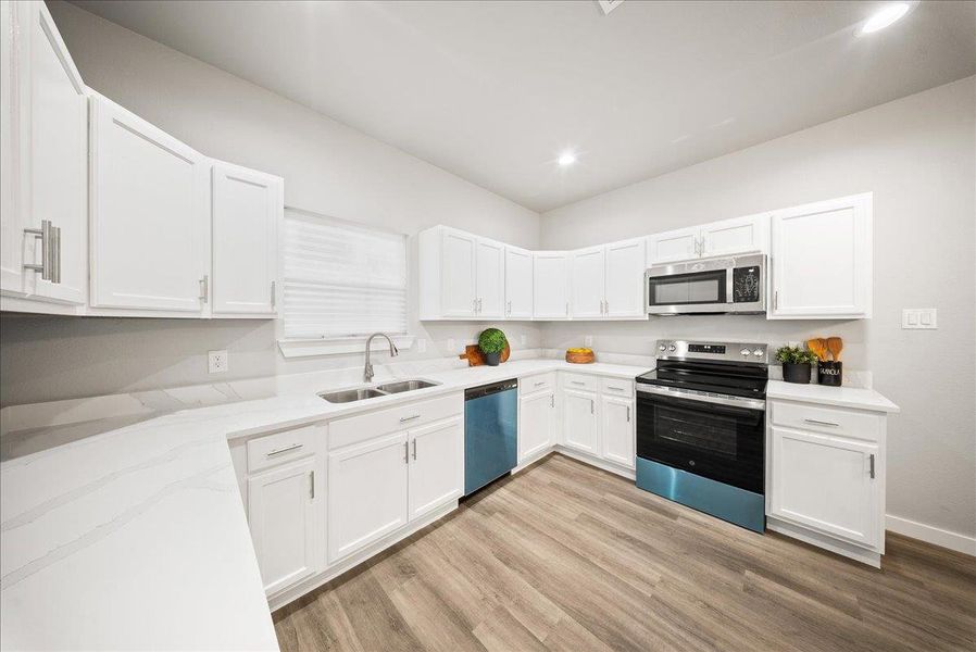 Kitchen with stainless steel appliances, light wood-type flooring, white cabinetry, light stone countertops, and recessed lighting Kitchen with stainless steel appliances, light wood-type flooring, white cabinetry, light stone countertops, and recessed lighting