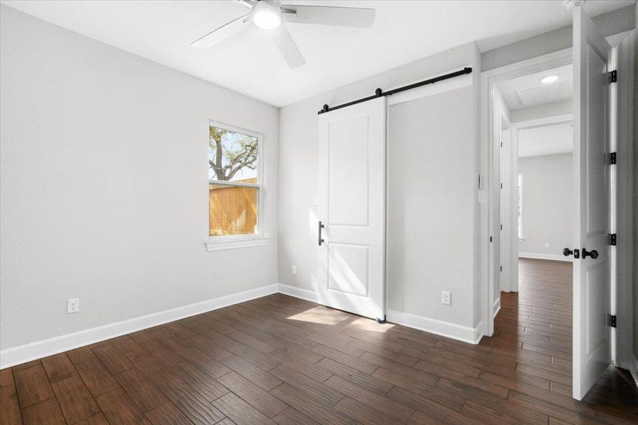 Unfurnished bedroom with dark wood-type flooring, a barn door, baseboards, and ceiling fan Unfurnished bedroom with dark wood-type flooring, a barn door, baseboards, and ceiling fan