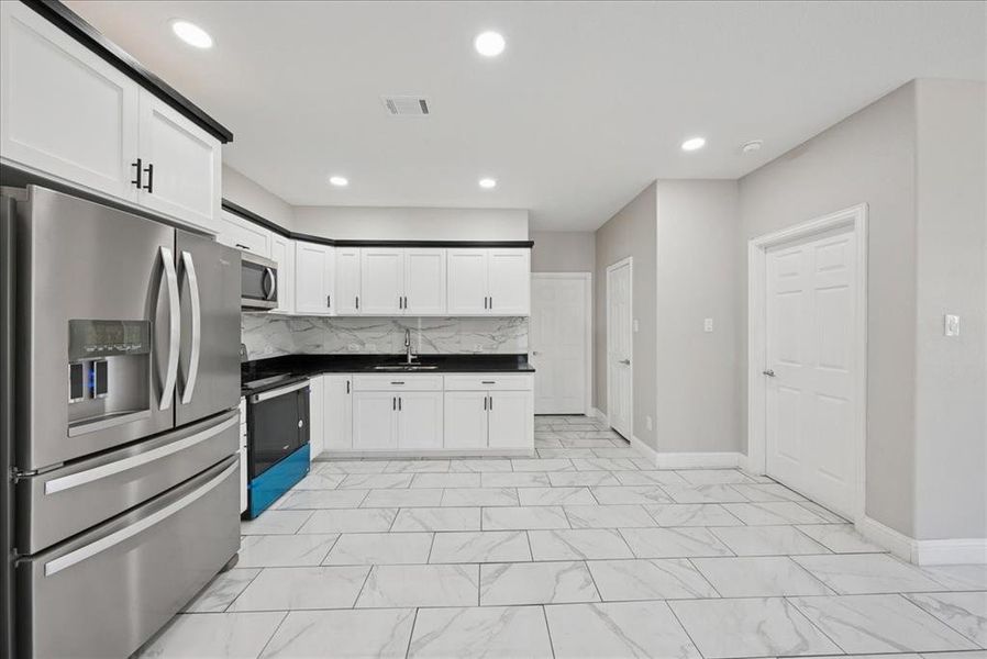 Kitchen with appliances with stainless steel finishes, tasteful backsplash, white cabinetry, recessed lighting, and light marble finish floors