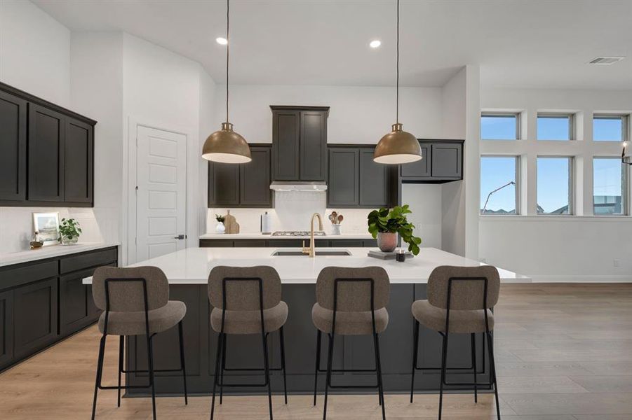 Kitchen featuring a kitchen bar, light wood-type flooring, a center island with sink, and pendant lighting