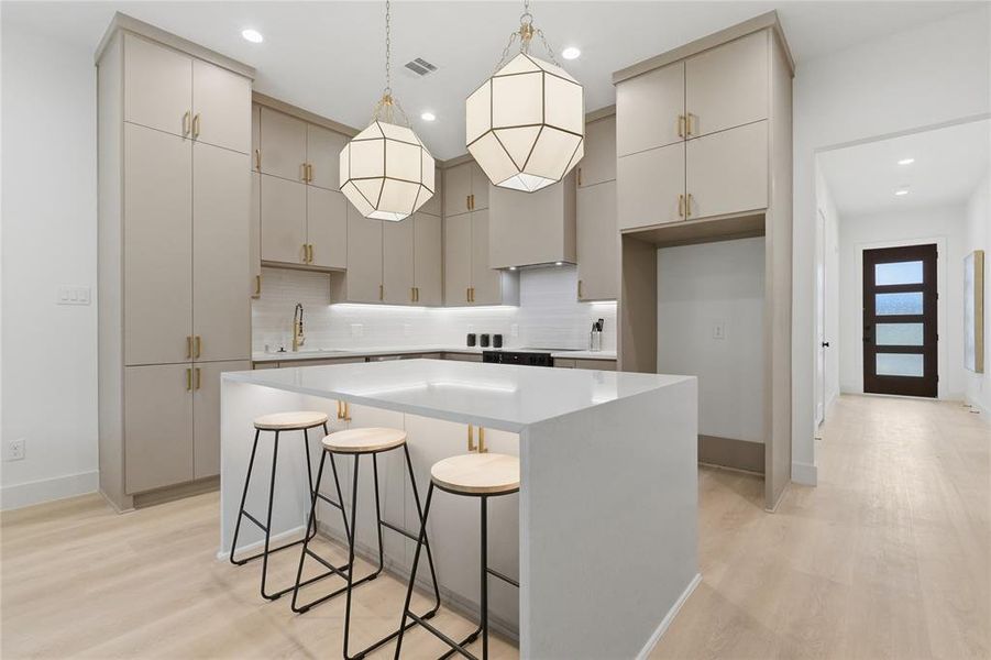 Modern kitchen featuring a large center island with integrated seating, extensive light-toned cabinetry, and sleek pendant lighting Modern kitchen featuring a large center island with integrated seating, extensive light-toned cabinetry, and sleek pendant lighting