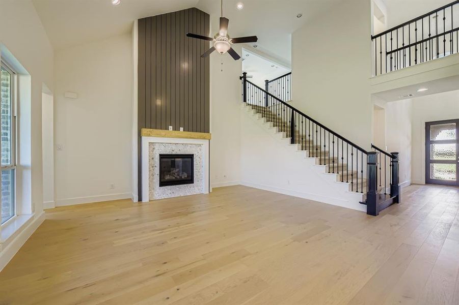 Unfurnished living room with high vaulted ceiling, a tiled fireplace, light wood-type flooring, recessed lighting, and stairway