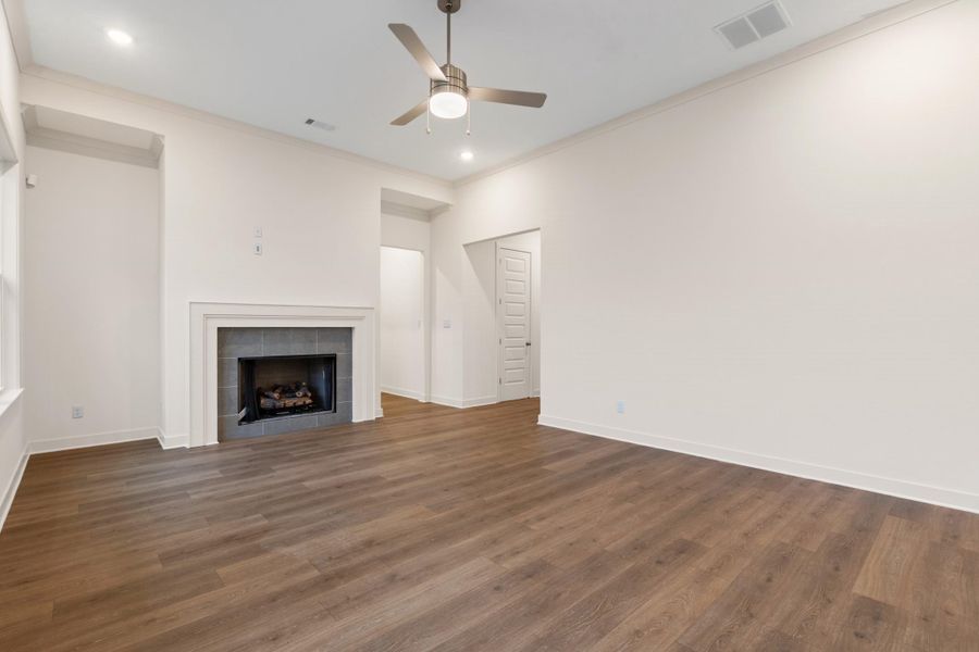 Spacious living area featuring a fireplace with a tiled surround and mantel, wood-finish flooring, recessed lighting, a ceiling fan, and white baseboards Spacious living area featuring a fireplace with a tiled surround and mantel, wood-finish flooring, recessed lighting, a ceiling fan, and white baseboards