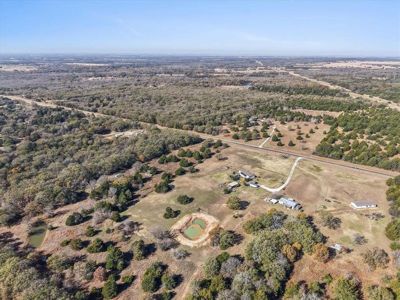 Expansive rural property featuring multiple structures, two ponds, mature trees, and a winding gravel drive