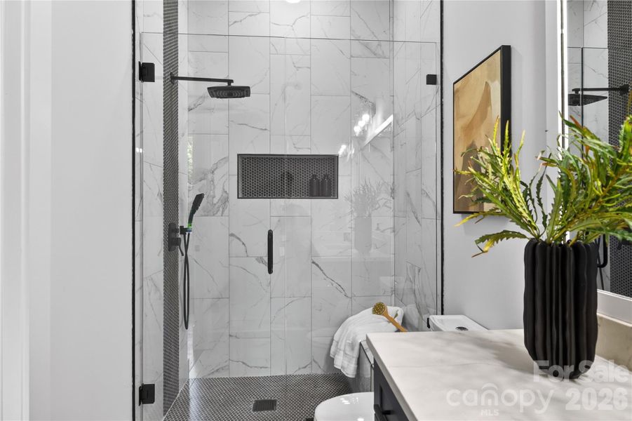 A fully tiled walk-in shower with frameless glass doors and designer finishes that make the space feel straight out of a luxury hotel