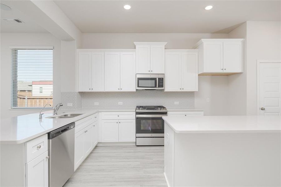 Kitchen with decorative backsplash, appliances with stainless steel finishes, white cabinetry, light hardwood / wood-style floors, and sink