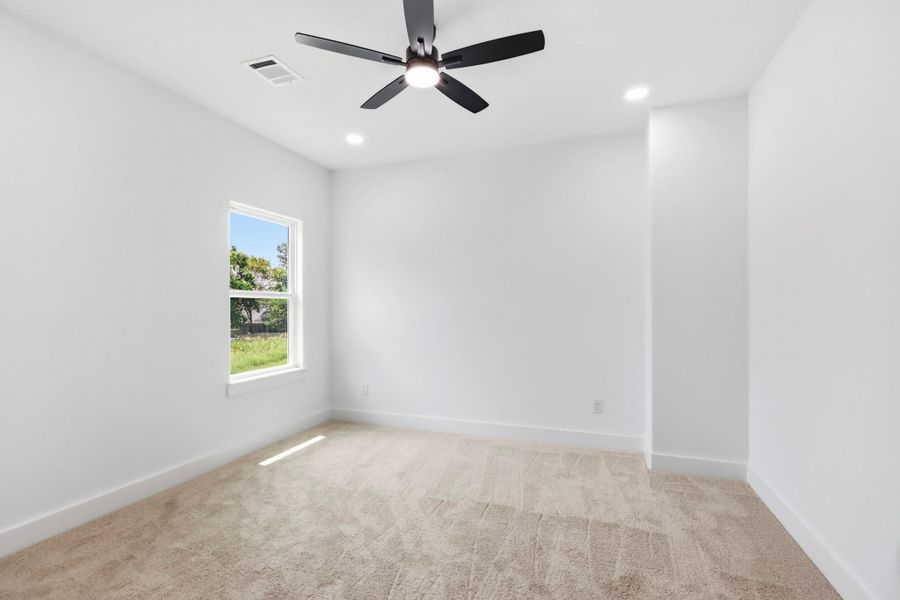 Bright and inviting bedroom featuring plush carpet, a modern ceiling fan, and a large window offering plenty of natural light.
