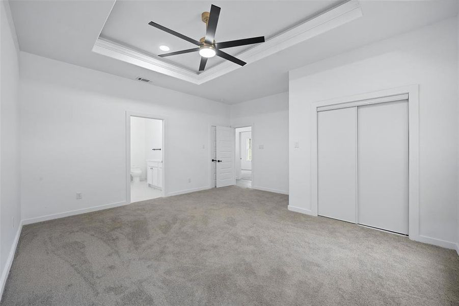 Unfurnished bedroom featuring a raised ceiling, light colored carpet, ornamental molding, ceiling fan, and a closet Unfurnished bedroom featuring a raised ceiling, light colored carpet, ornamental molding, ceiling fan, and a closet