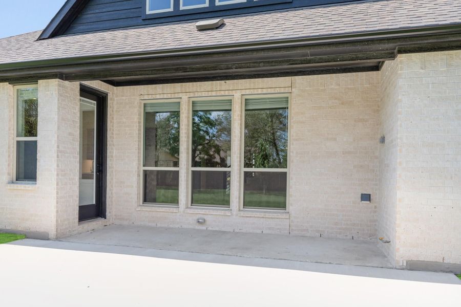 Exterior rear of home with light brick wall, three large windows, black door, and concrete patio