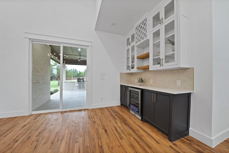Living area featuring hardwood flooring, a built-in wet bar with a wine refrigerator, and glass-front upper cabinetry