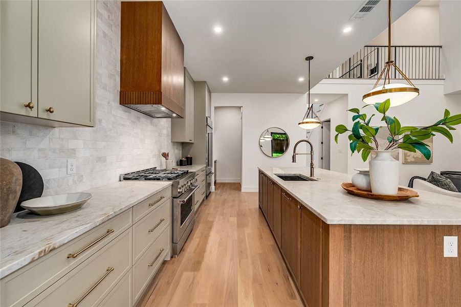 Kitchen with light stone countertops, premium appliances, light wood-type flooring, hanging light fixtures, and brown cabinets Kitchen with light stone countertops, premium appliances, light wood-type flooring, hanging light fixtures, and brown cabinets