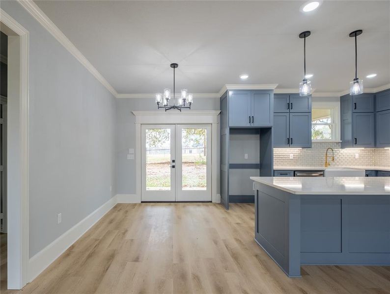 Kitchen featuring blue cabinetry, hanging light fixtures, ornamental molding, light stone countertops, and a chandelier Kitchen featuring blue cabinetry, hanging light fixtures, ornamental molding, light stone countertops, and a chandelier