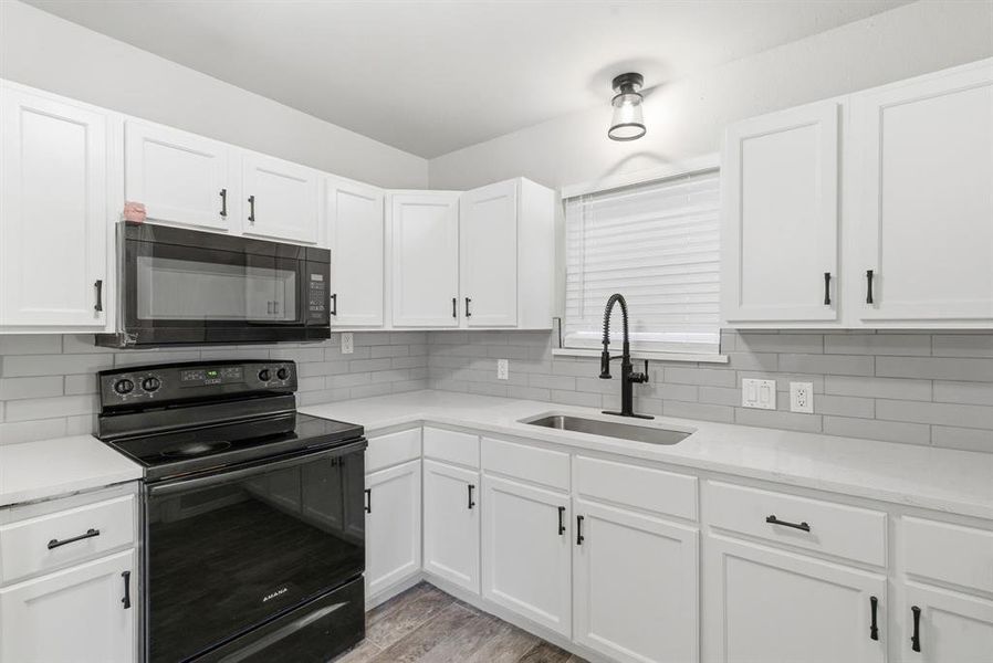 Kitchen with black appliances, white cabinets, light stone counters, and light wood finished floors Kitchen with black appliances, white cabinets, light stone counters, and light wood finished floors