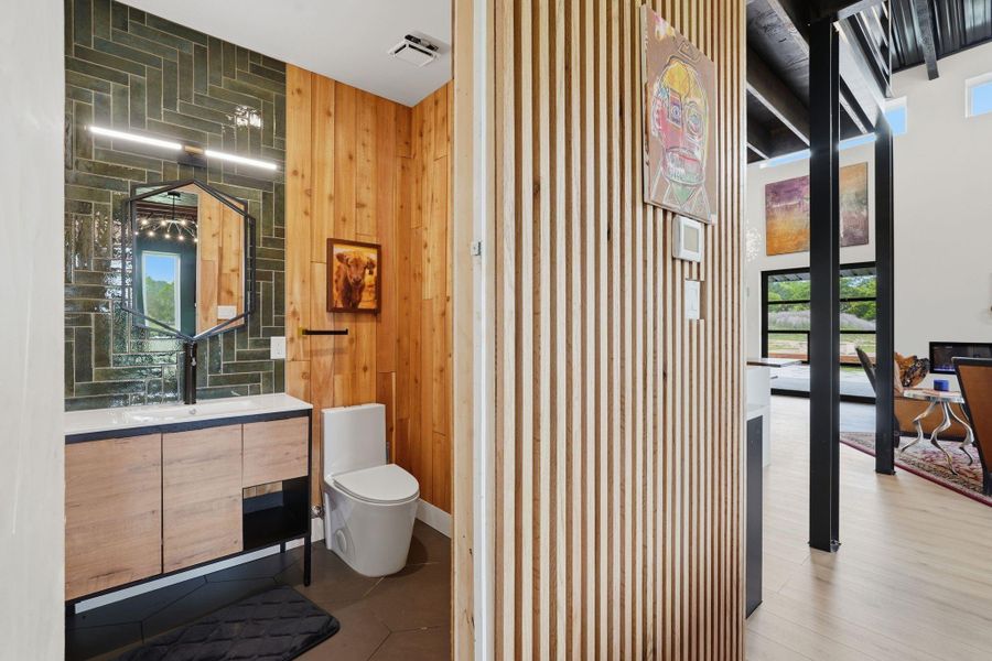 This photo showcases a modern bathroom with wood paneling and a unique geometric mirror, adjacent to an open living space featuring large windows and contemporary decor.