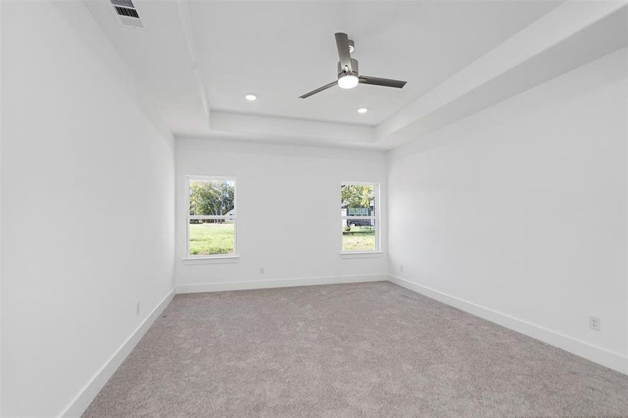 Empty room featuring ceiling fan, a raised ceiling, and light carpet