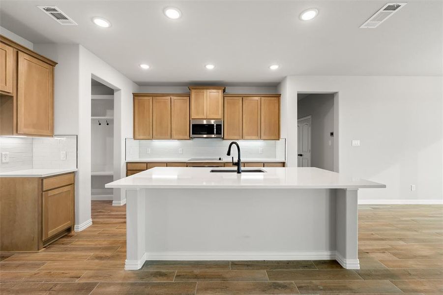 Kitchen with decorative backsplash, an island with sink, light stone countertops, brown cabinets, and recessed lighting Kitchen with decorative backsplash, an island with sink, light stone countertops, brown cabinets, and recessed lighting
